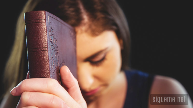 Mujer joven orando a Dios con la Bilia entre sus manos