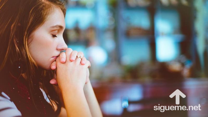 Joven cristiana orando de rodillas a Dios