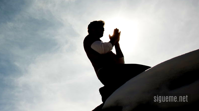 Joven cristiano arrodillado orando a Dios sobre una cima