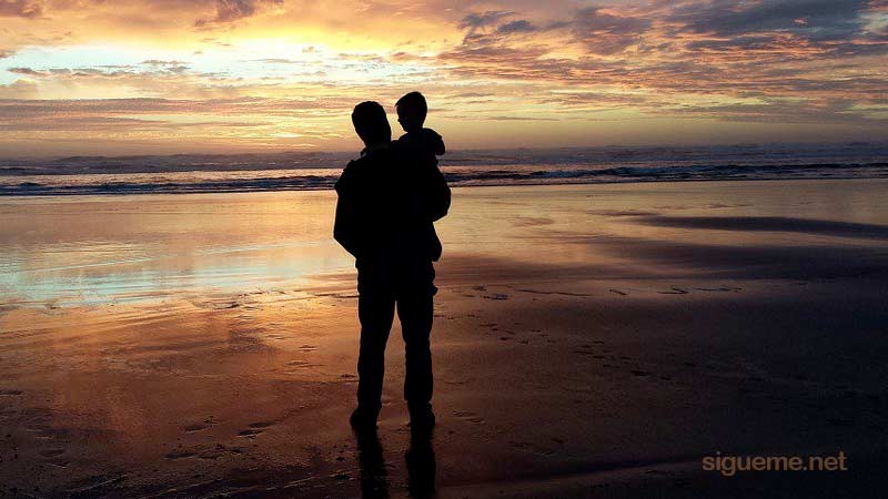 Papa con su hijo en brazos frente al mar al amanecer