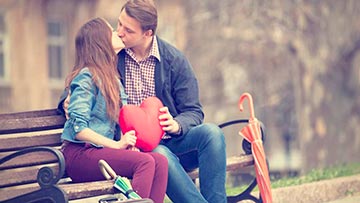 novios cristianos enamorados besandose en un banco de plaza