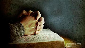 Orando a Dios con las manos sobre la Biblia abierta