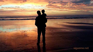 Papa con su hijo en brazos frente al mar al amanecer